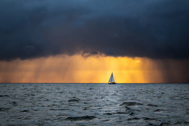Boat sailing into the storm Lonely sailing yacht in the ocean at the approaching storm and raining clouds at sunrise, English channel, near French shores atlantic ocean photos stock pictures, royalty-free photos & images
