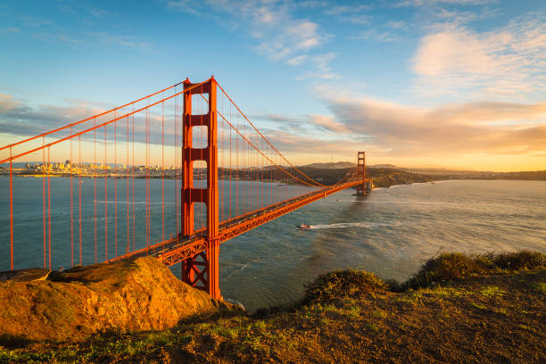 Sunset at the Golden Gate Bridge View at the Golden Gate Bridge and downtown San Francisco with clouds and with a boat under the bridge in December san francisco california stock pictures, royalty-free photos & images