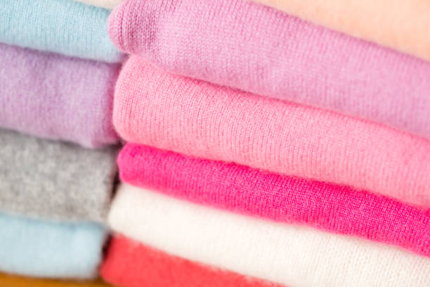 Stack of warm pink, purple, white, light blue, grey, red and orange cozy sweaters.