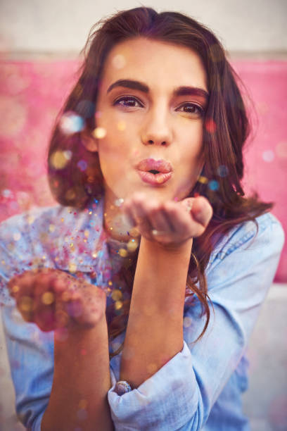 Portrait of a beautiful young woman blowing confetti outside