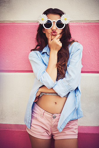 Cropped shot of a beautiful young woman wearing novelty sunglasses and posing against a wall outside