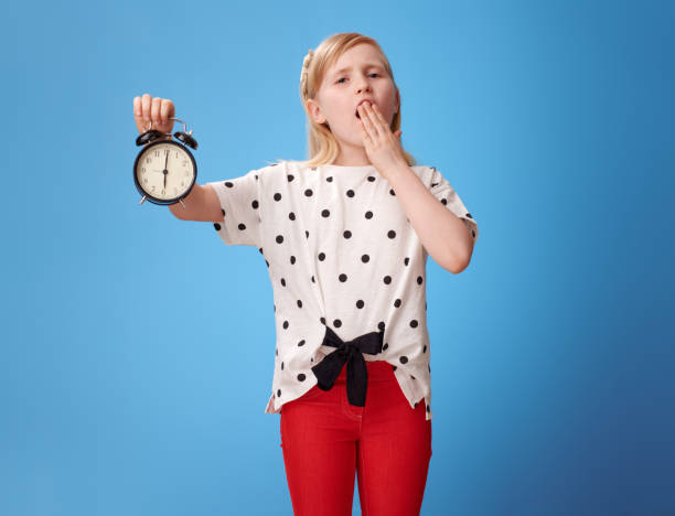 istock modern child showing alarm clock and yawing on blue 965455278