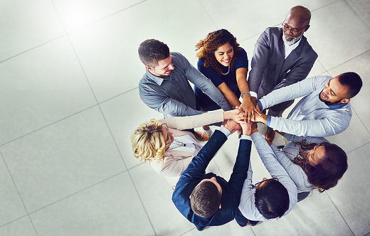 High angle shot of a group of businesspeople joining hands together in solidarity in a modern office