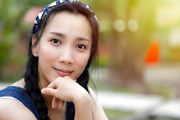 young asian smiling woman tied with braids at outdoors portrait; Soft sunny colors.
