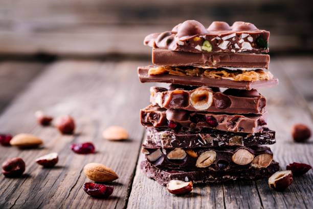 우유와 견과류, 카라멜과 과일, 열매 나무 배경에 다크 초콜릿의 스택. - chocolate 뉴스 사진 이미지