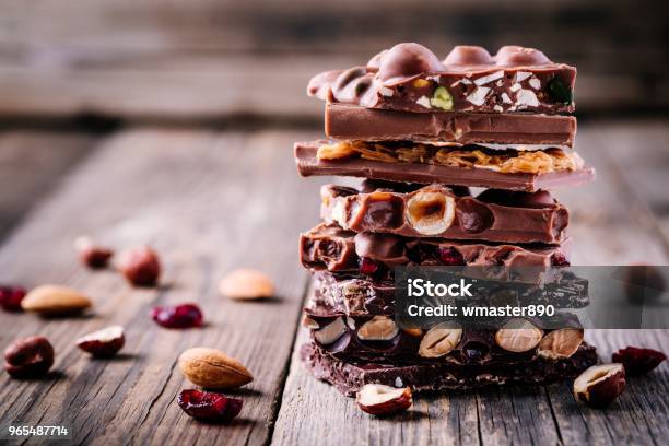 Stack Of Milk And Dark Chocolate With Nuts Caramel And Fruits And Berries On Wooden Background Stock Photo - Download Image Now