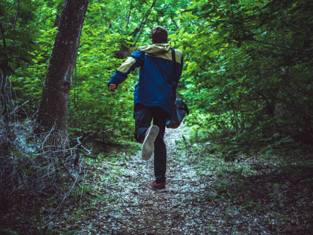 giovane uomo spaventoso in esecuzione nella foresta buia sul sentiero retro vista - escape foto e immagini stock