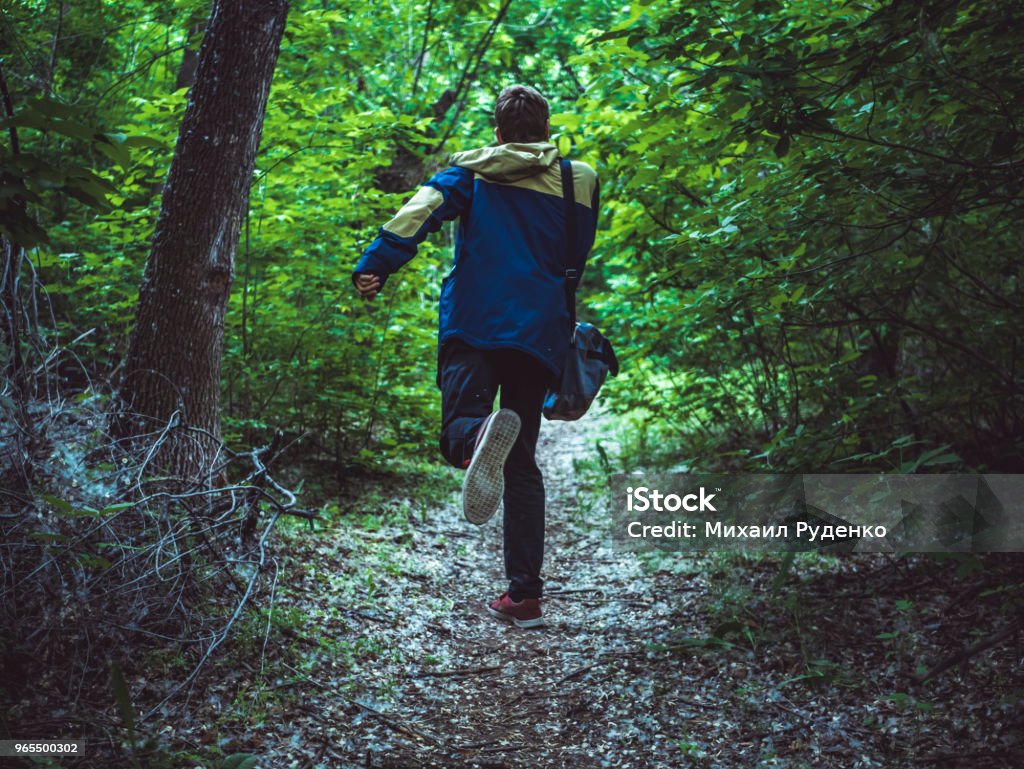 young scary man running away in the dark forest on the path back view Escaping Stock Photo