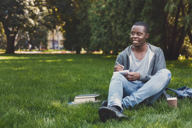 Young man writing in copy-book outdoors