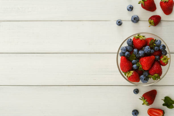 istock Mixed berries in glass bowls on white wooden table top view 965503064