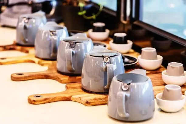 Many tea pots are assembled in a display row on wooden chopping boards in the window of a cafe