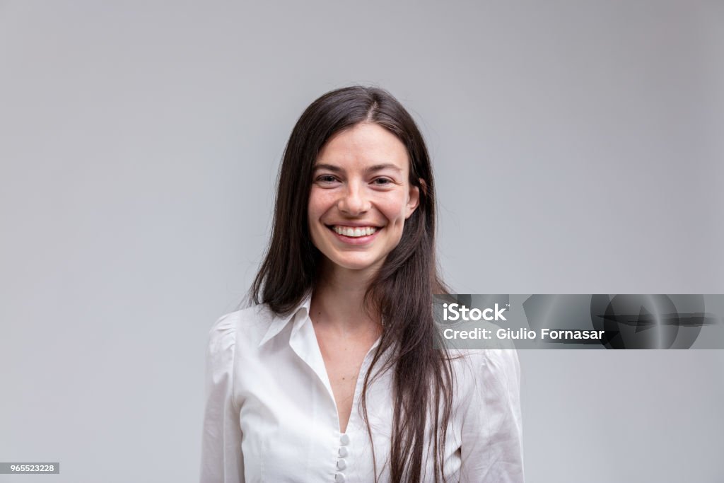 Young long-haired smiling woman in white shirt Portrait of young long-haired cheerful woman wearing white shirt against plain background Portrait Stock Photo