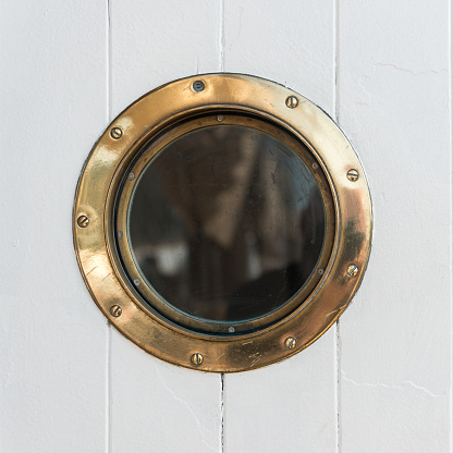 A brass porthole, white wooden background