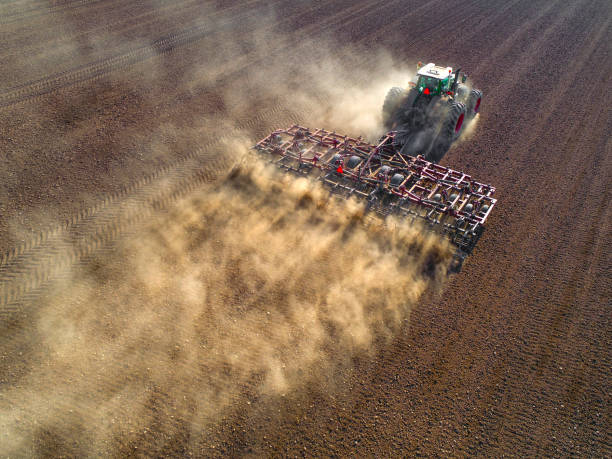 Big farm tractor tilling dusty Springtime fields. stock photo