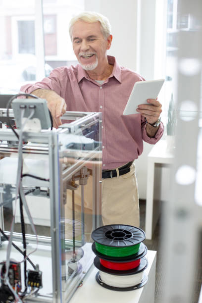 Joyful senior man learning how to use 3D printer Good results. Upbeat senior man learning how to use a 3D printer and smiling cheerfully while checking its settings 3d printing photos stock pictures, royalty-free photos & images
