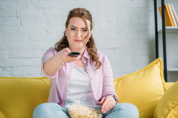 istock beautiful woman changing tv channels with remote control at home 965556814