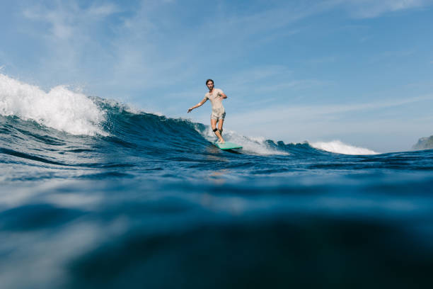 istock handsome man in wet t-shirt riding waves on surfboard on sunny day 965560436