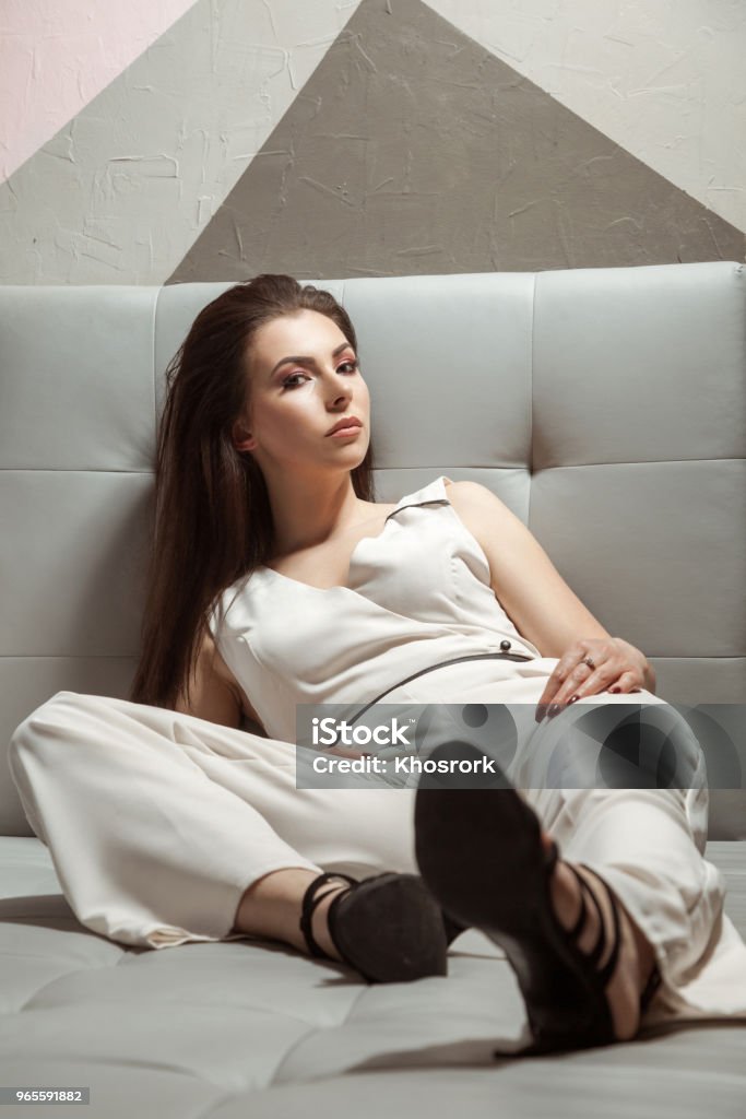 Beautiful Woman In White Stylish Classic Overalls Relaxing On Sofa Stock Photo - Download Image Now - iStock