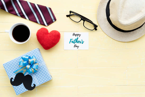 istock Happy fathers day concept. Red tie, glasses, hat, mustache, gift box with Love DAD text on black heart tag on bright yellow pastel wooden table background. 965601622