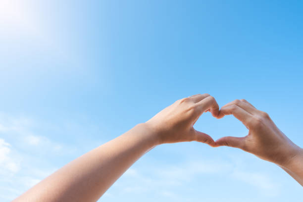 istock Female hands in heart shape over blue sky background in sunny day. 965666236
