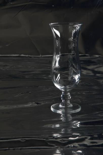istock Still life with one single modern transparent and fragile (cocktail) glass on a table with a black background 965668866