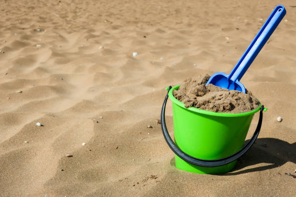 Play in sand.  Green plastic bucket and blue shovel