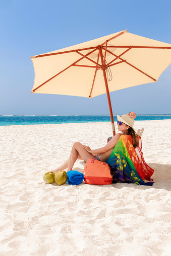 Hispanic Young woman relaxing under beach umbrella on a tropical white sand island beach in the Caribbean sea