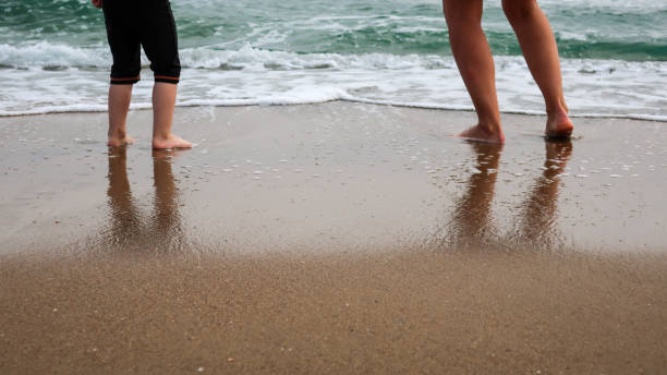 Mother and daughter play at the beach. Reflections in wet sand. Concept for traveling with children / family vacation and holiday.