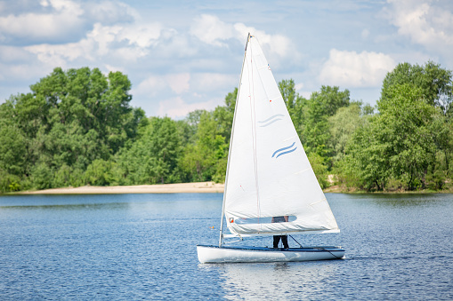 Landscape of lake with white yacht on bright sunny summer day. Blue sky with white clouds over big lakes and green trees and hills on horizon.