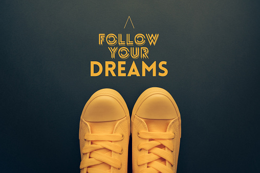 Follow your dreams motivational quote, young person in yellow casual canvas shoes standing over the text