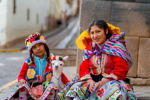 young woman with her little niece pose in a portrait with their typical costumes next to her little alpaca in a street in the historic center of cusco - india traditional culture indigenous culture women imagens e fotografias de stock