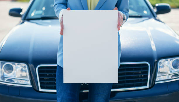 istock Woman standing by car holding a white blank poster 965715218