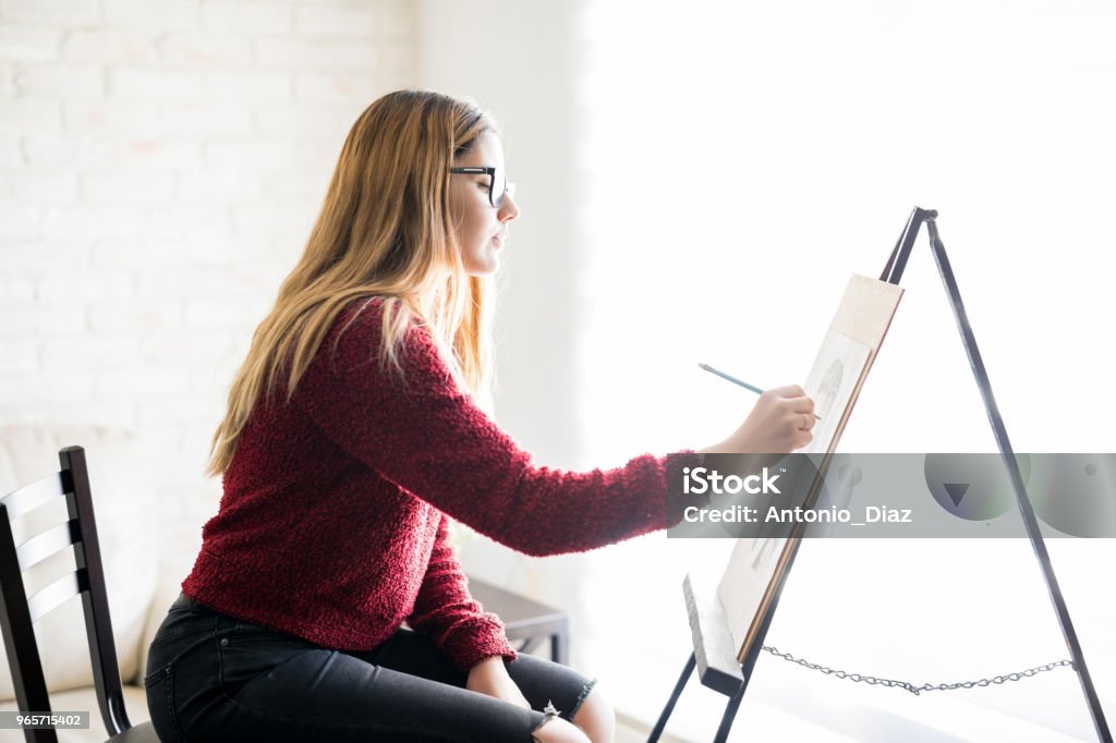 Woman artist doing canvas painting Profile view of cute young female painter doing some painting on canvas 20-29 Years Stock Photo