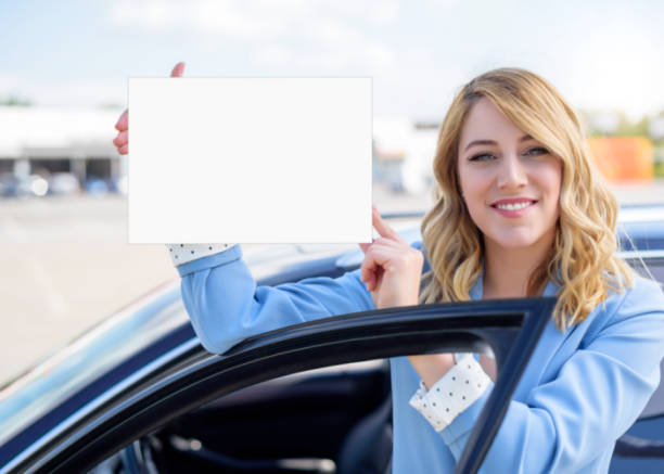 istock Woman standing by car holding a white blank poster 965718534