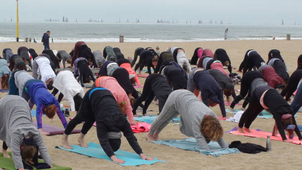 un sacco di persone che fanno esercizio yoga per la salute e il relax sulla spiaggia - lying down moving down pilates yoga foto e immagini stock