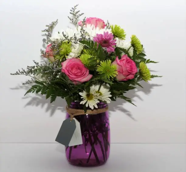 Arrangement of spring flowers in a purple vase with a white background