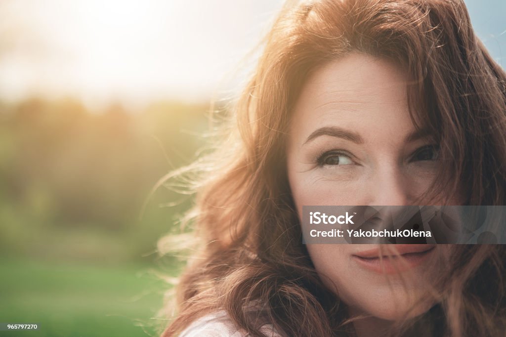 Happy red-haired lady enjoying every moment in nature Natural beauty. Close up portrait of dreamful woman with red curly hair. She is looking aside with enjoyment and smiling while resting in the fresh air. Copy space Women Stock Photo