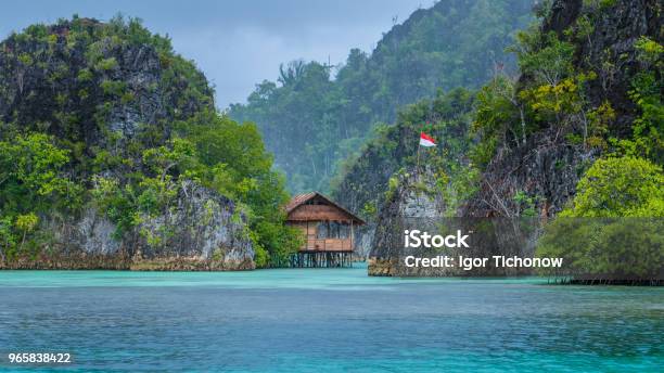 Bamboo Hut Between Some Rocks Under Rain In Bay With Indonesian Flag Pianemo Islands Raja Ampat West Papua Indonesia Stock Photo - Download Image Now