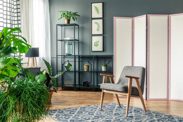 uno schermo decorativo accanto agli scaffali neri e dietro una sedia grigia in piedi su un tappeto a motivi geometrici con piante intorno all'interno di una stanza botanica - separè foto e immagini stock