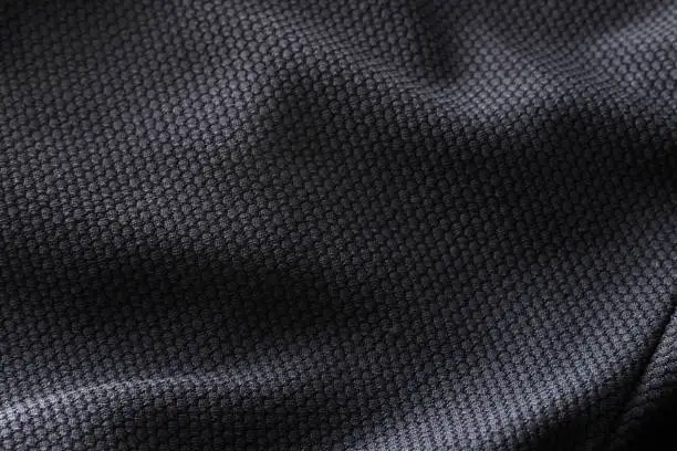 Close-up polyester fabric texture of black athletic shirt with ambient light