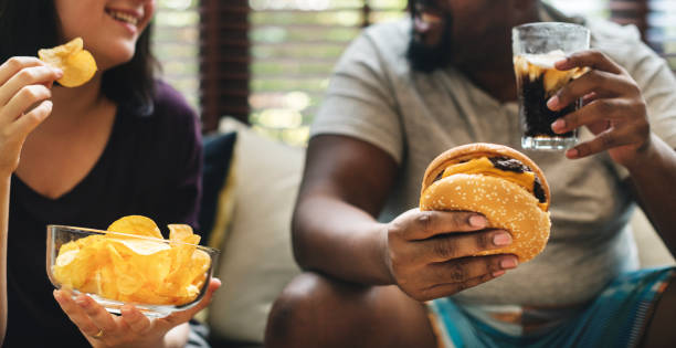 pareja de comida rápida en el sofá - modo de vida no saludable fotografías e imágenes de stock