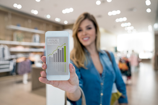 Portrait of a business owner showing statistics on a cell phone at a clothing store. **DESIGN ON SCREEN WAS MADE FROM SCRATCH BY US**