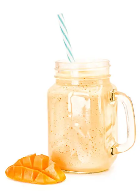 Photo of mango milkshake in mason jar with blue and white drinking straw decorated with mango half isolated on white background