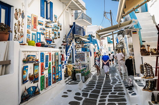 Mykonos, Greece-May 8, 2018-Shoppers explore the narrow alleys of Mykonos Town where colorful merchandise is displayed in hopes of catching  a tourists eye.
