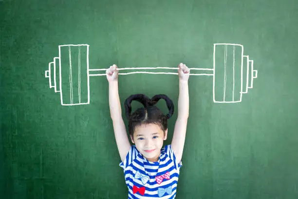 Happy healthy strong kid weight lifting on grunge green chalkboard background: International day of girl child Equality opportunity awareness on women human rights Children's day concept Leader idea