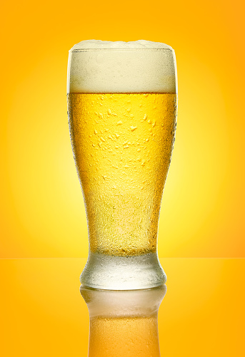 cold beer in glass on yellow background