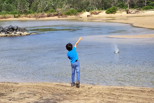 Kid throwing stone in water. Child in action of throwing rock or stone in water.
