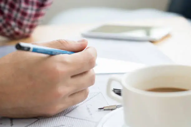 Photo of An engineer work for architectural project.With a cup of coffee,tools,drawing and white helmet on work table at home office.selective focus