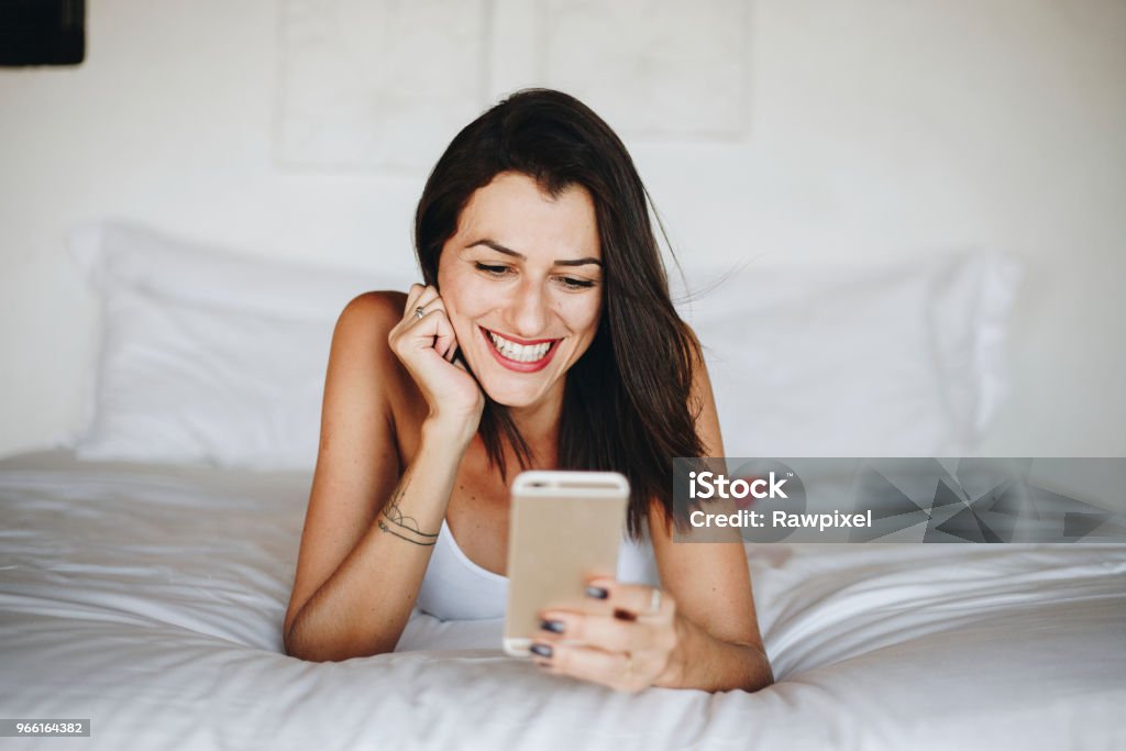 Donna che usa un cellulare a letto - Foto stock royalty-free di Adulto