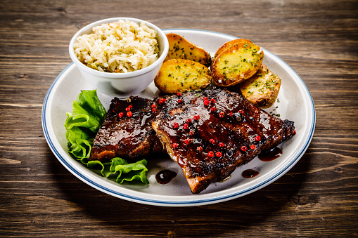 Grilled ribs, baked potatoes and vegetables on wooden background
